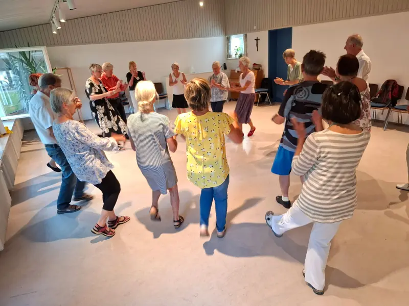 Eine große Gruppe aus Frauen und Männern tanzt und klatscht im Gemeindehaus Füssen